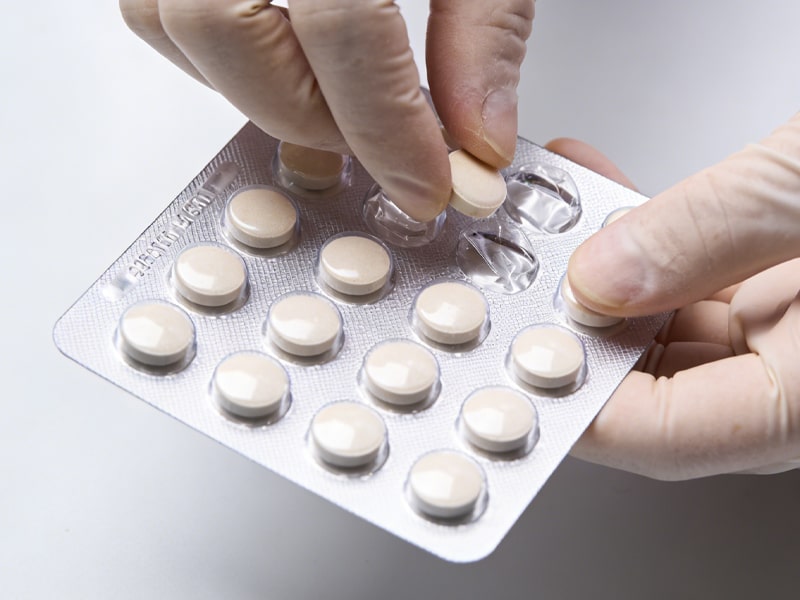 Die Hand eines Technikers holt eine Tablette aus einer durchsichtigen Plastikblisterpackung