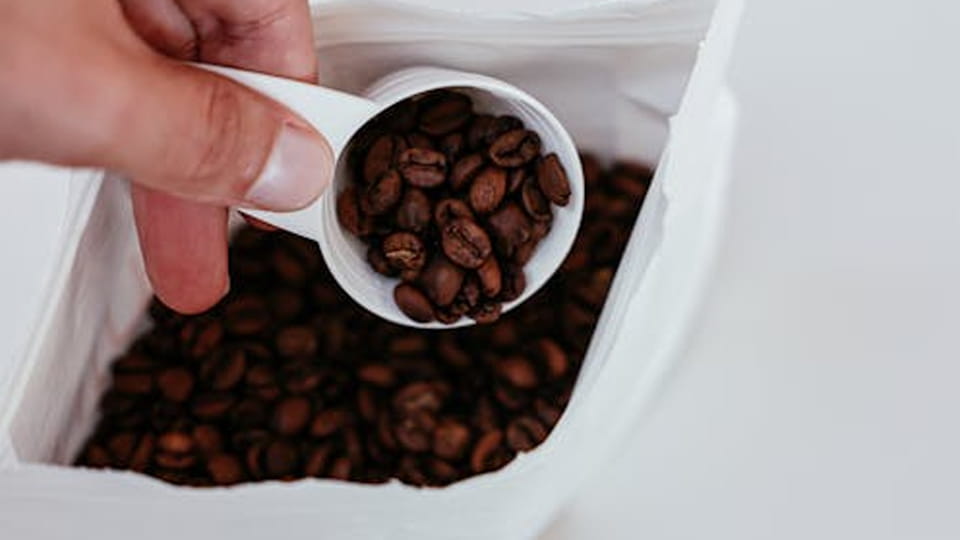 A spoon scoops coffee beans from the pouch