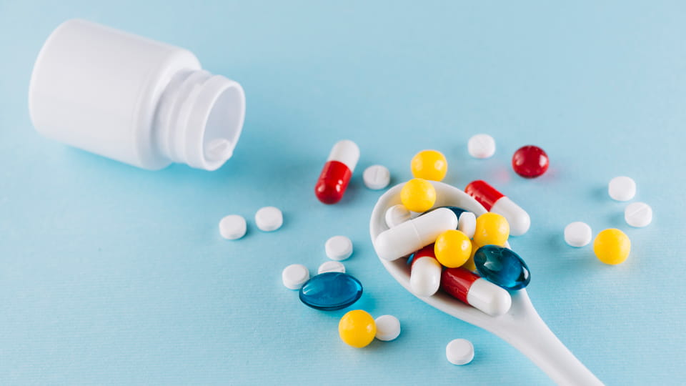 tablets and capsules on spoon with pill bottle