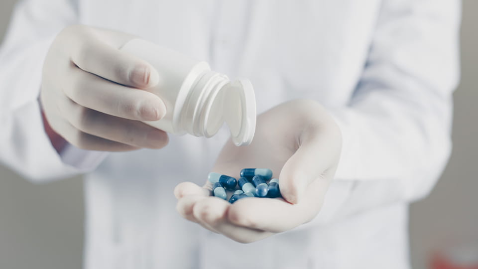 worker with gloves holding finished capsules and bottle