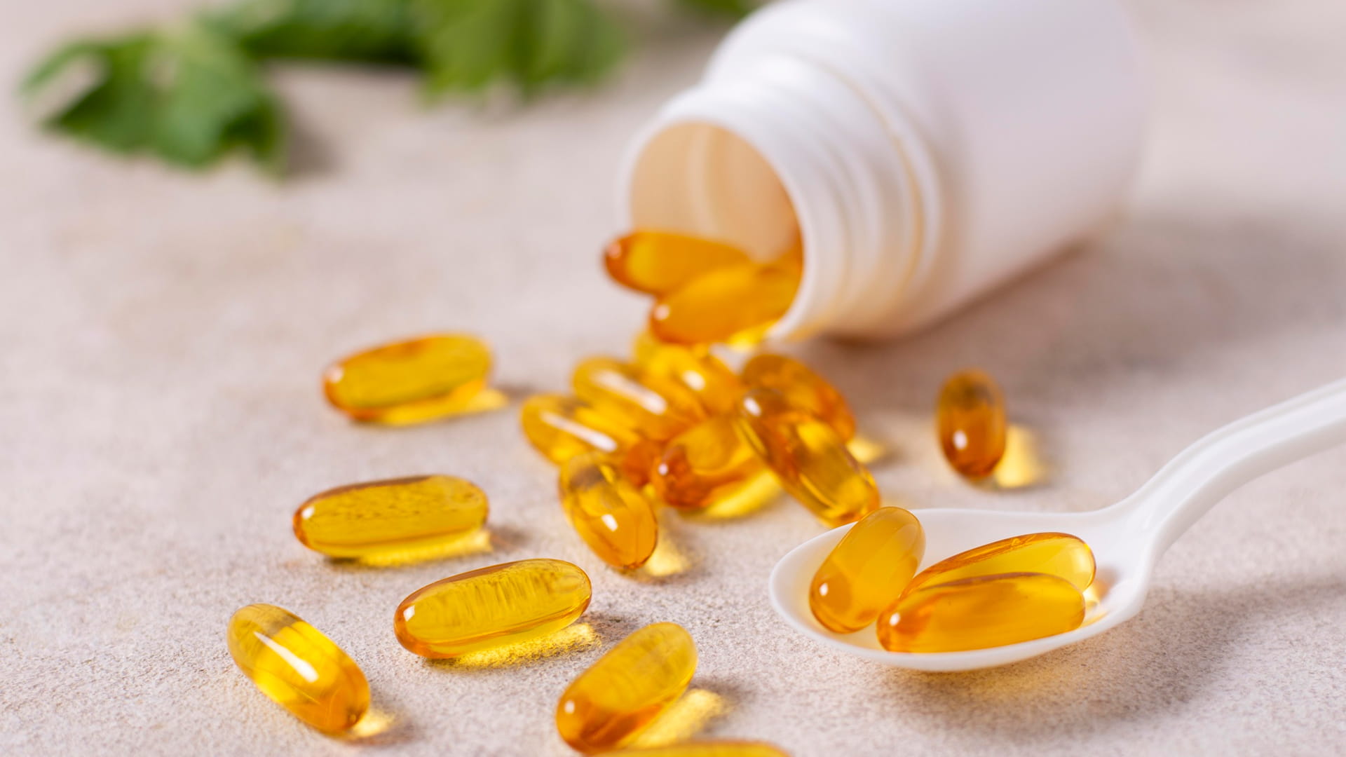 Amber softgel capsules on a teaspoon next to a pill bottle