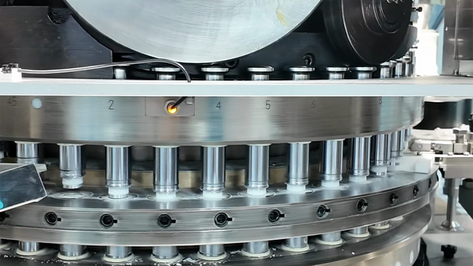 Rotary tablet press showing punch heads and compression rollers during dwell time in tablet compression