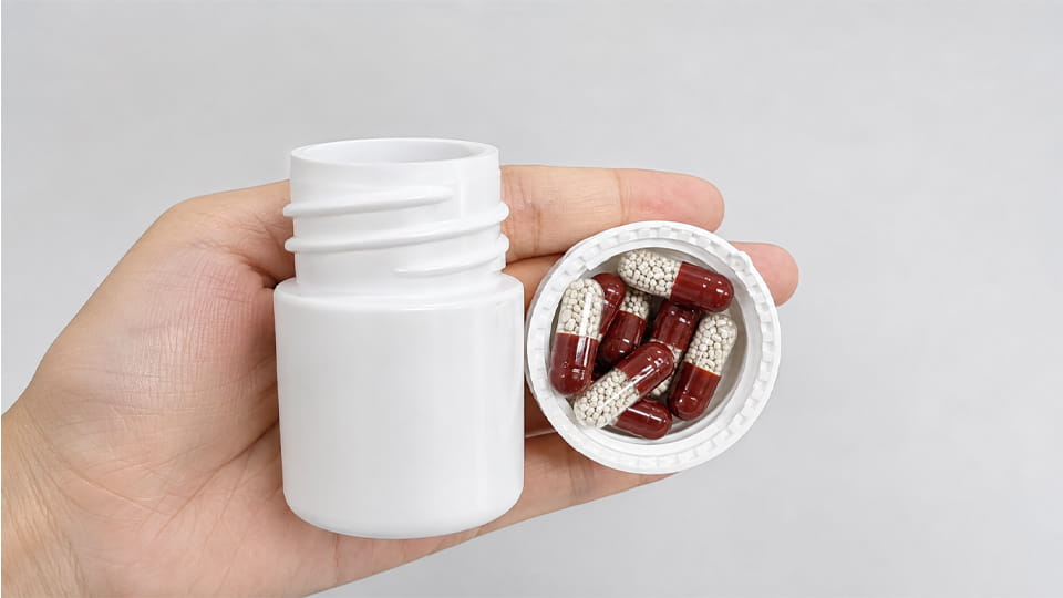 Alt: Enteric capsules filled with pellets in an open white medicine bottle