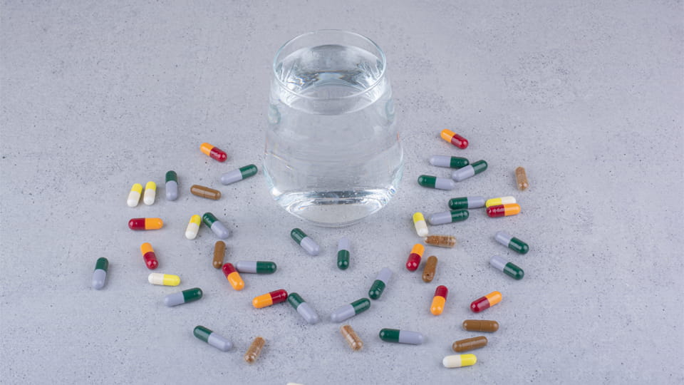 Various pharmaceutical capsules scattered around a glass of water, illustrating capsule formulations and shell materials discussed in relation to capsule dissolution failure.