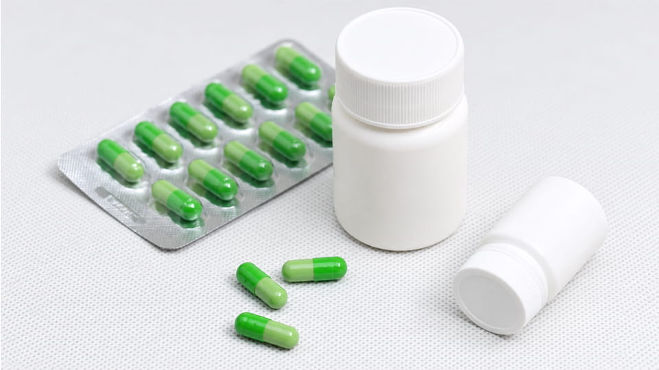 Green pharmaceutical capsules in blister packs and plastic bottles, illustrating packaging options that help protect capsule stability and reduce dissolution failure risks.