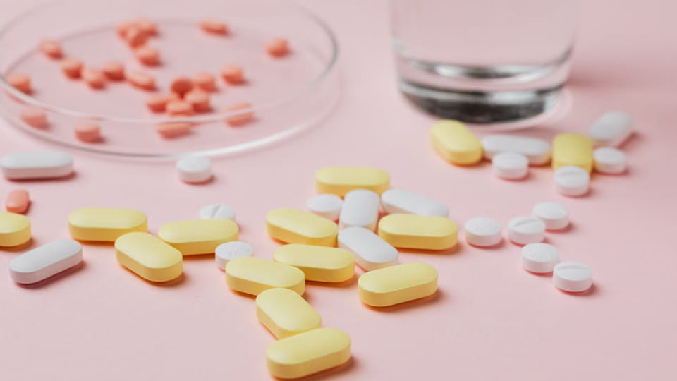 Assorted coated pharmaceutical tablets in different shapes, サイズ, and colors on a pink surface, illustrating tablet quality considerations for coating and packaging.