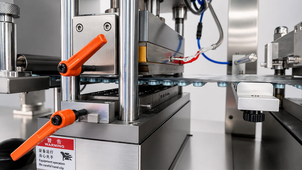 Close-up of a blister packaging machine heat sealing station, showing the sealing tooling and blister film during the heat-sealing process.