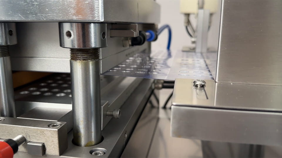 Close-up of a pharmaceutical blister packaging machine thermoforming station forming tablet cavities in packaging film.
