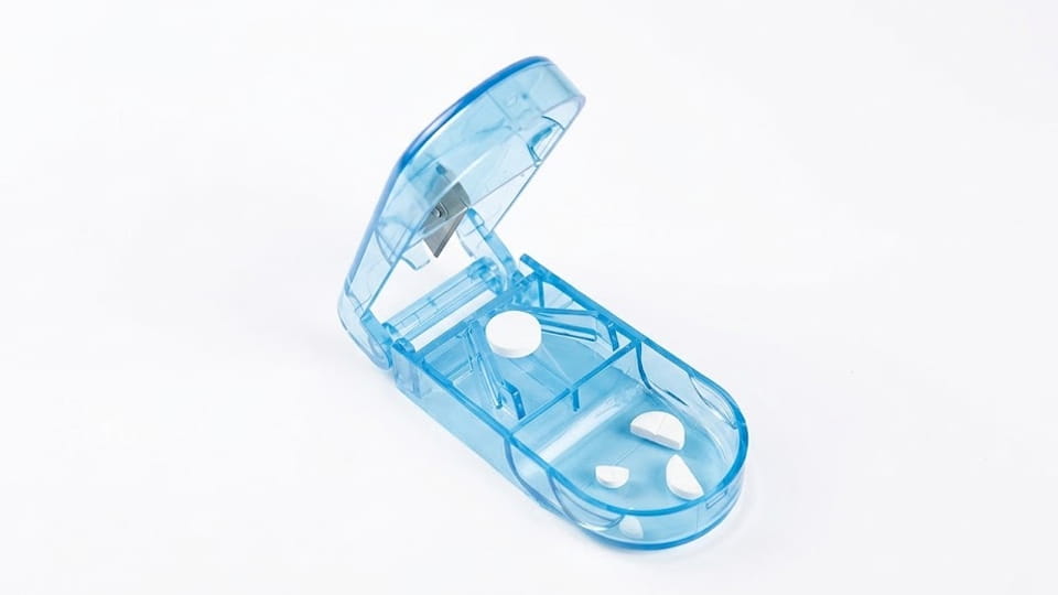 Blue manual pill cutter with scored tablets and split tablet pieces, illustrating controlled tablet splitting for repeatability testing.
