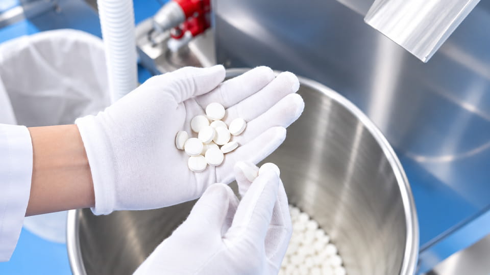 Gloved operator inspecting white tablets collected from a pharmaceutical tablet press during quality control sampling.