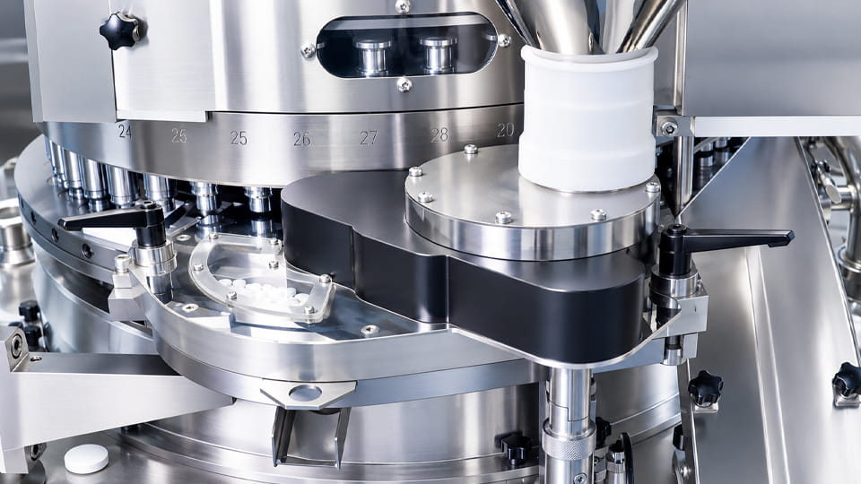 Close-up of a force feeder on a rotary tablet press, showing the stainless steel feeding components and tablet compression turret.